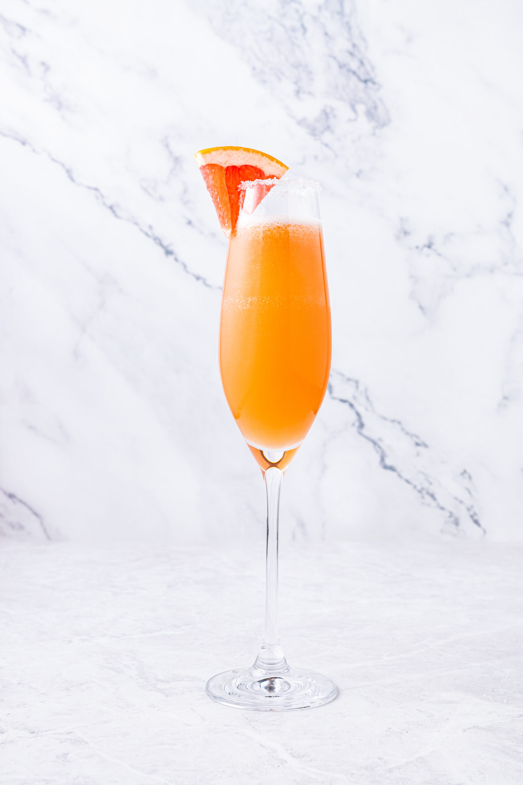 A Champagne Paloma cocktail in a flute glass, with a salted rim and grapefruit wedge.