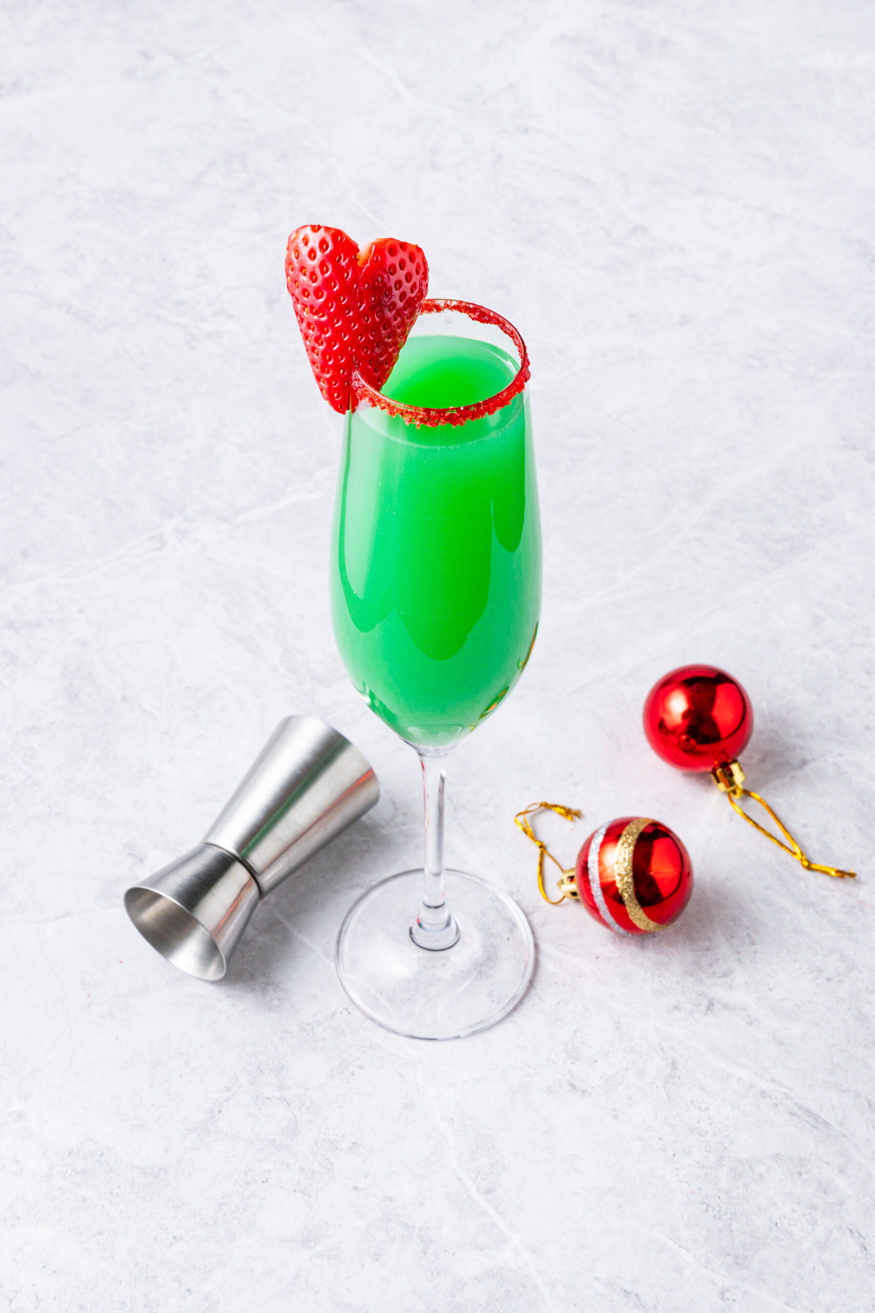 Grinch Mimosa cocktail in a champagne flute, green with a heart strawberry and red sugar rim.