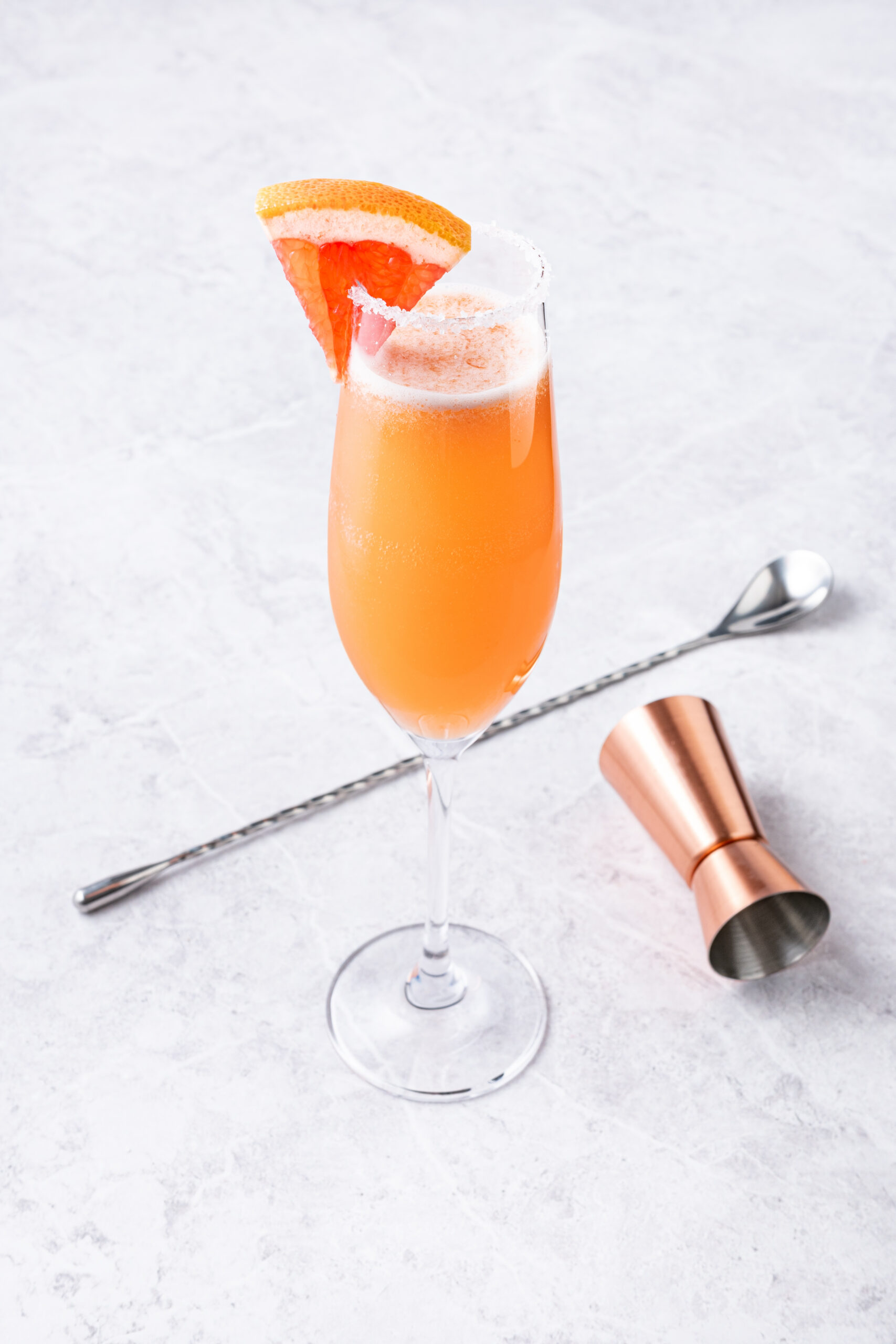 A Champagne Paloma cocktail in a flute glass with a salted rim and grapefruit wedge.