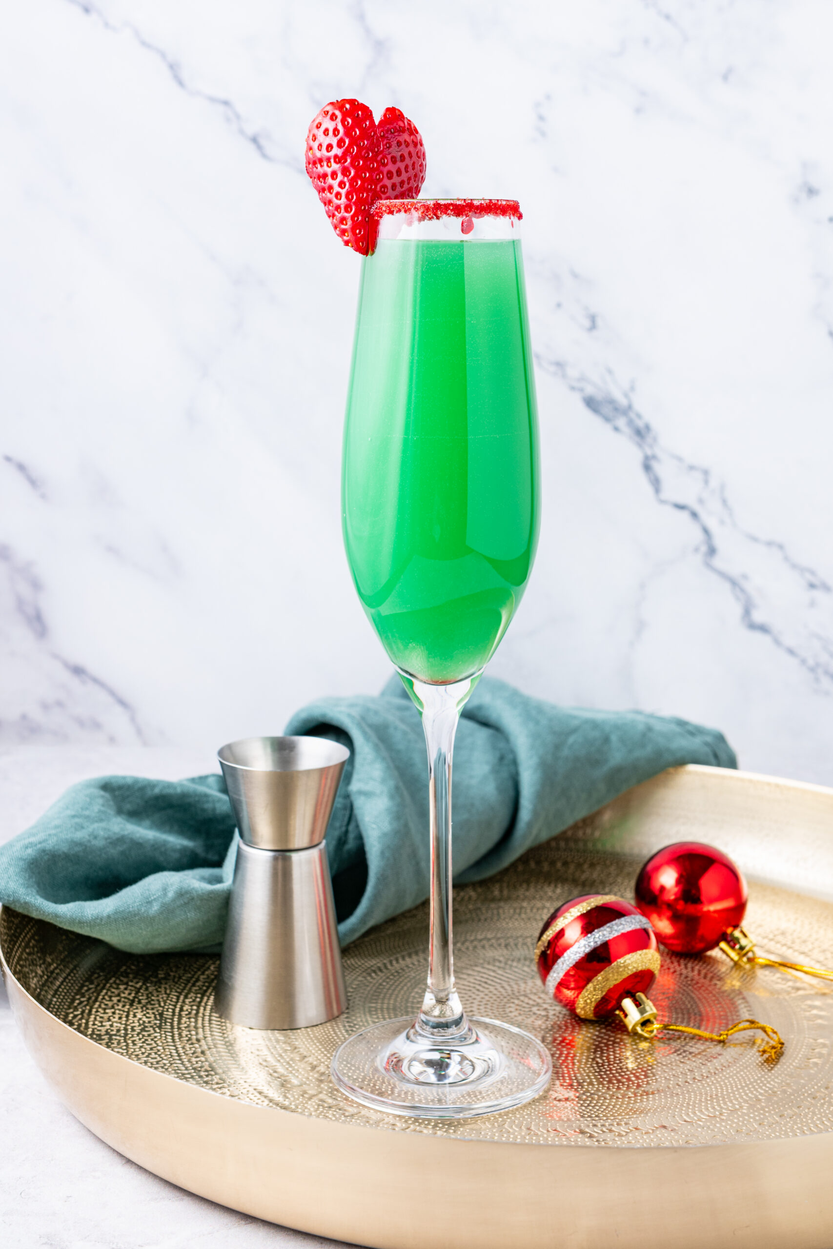A green Grinch Mimosa in a champagne flute, with a strawberry and red sugar rim.