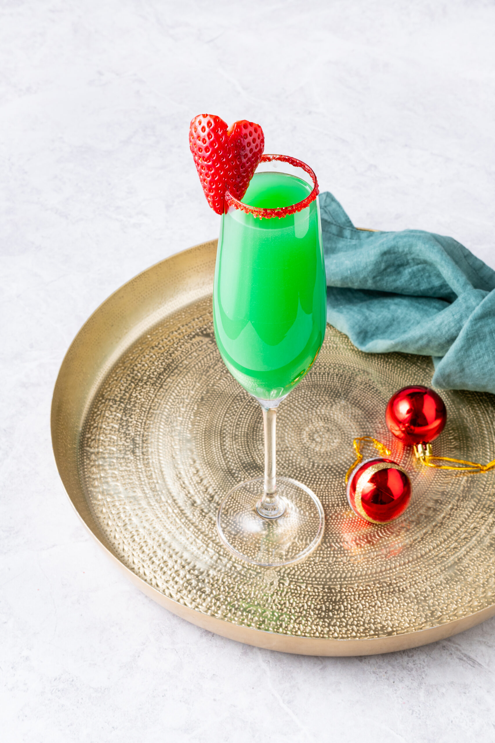 Grinch mimosa in a champagne flute, with a strawberry heart and red sugar rim.