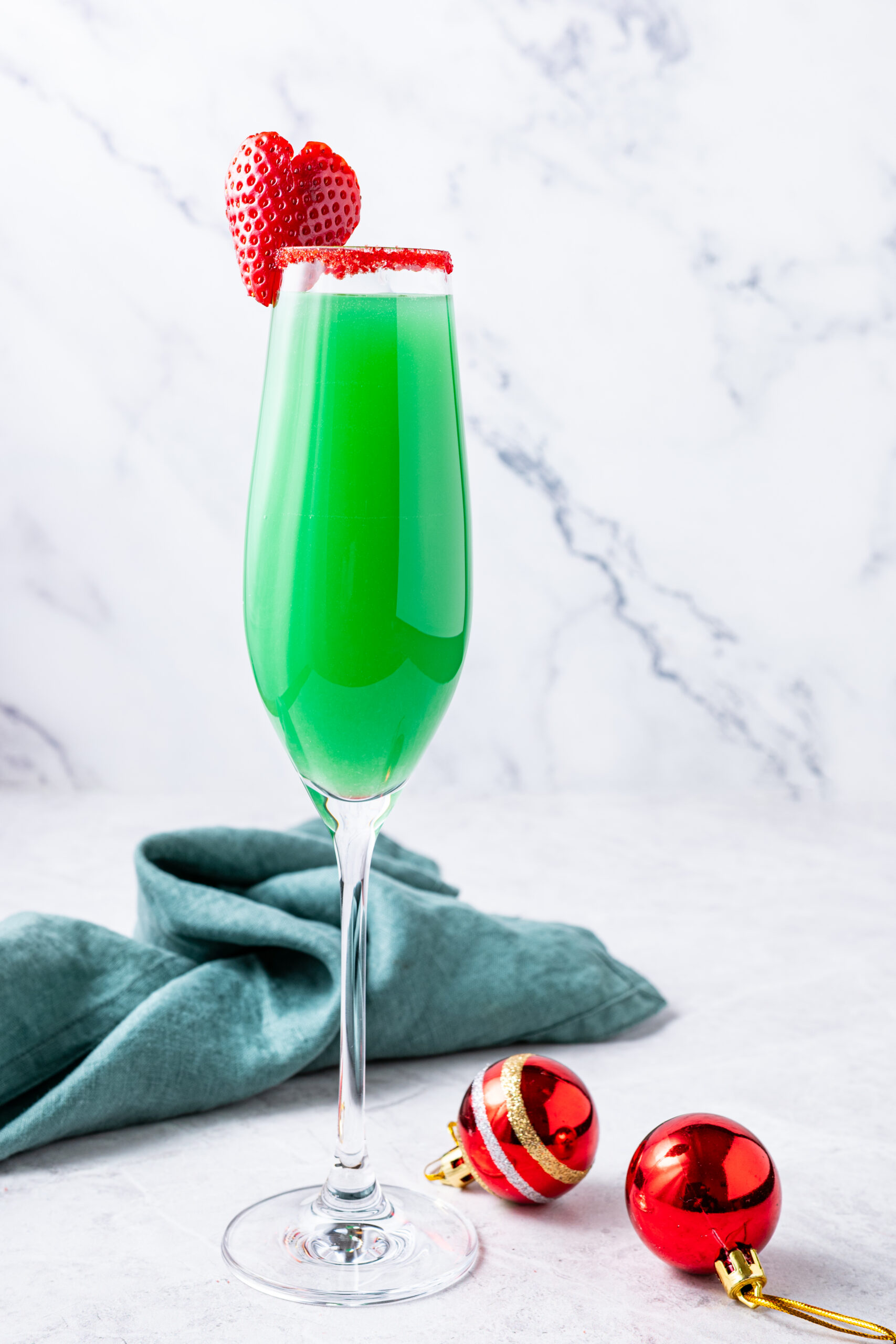 Grinch Mimosa in a champagne flute with a sugared rim, strawberry, and Christmas ornaments.