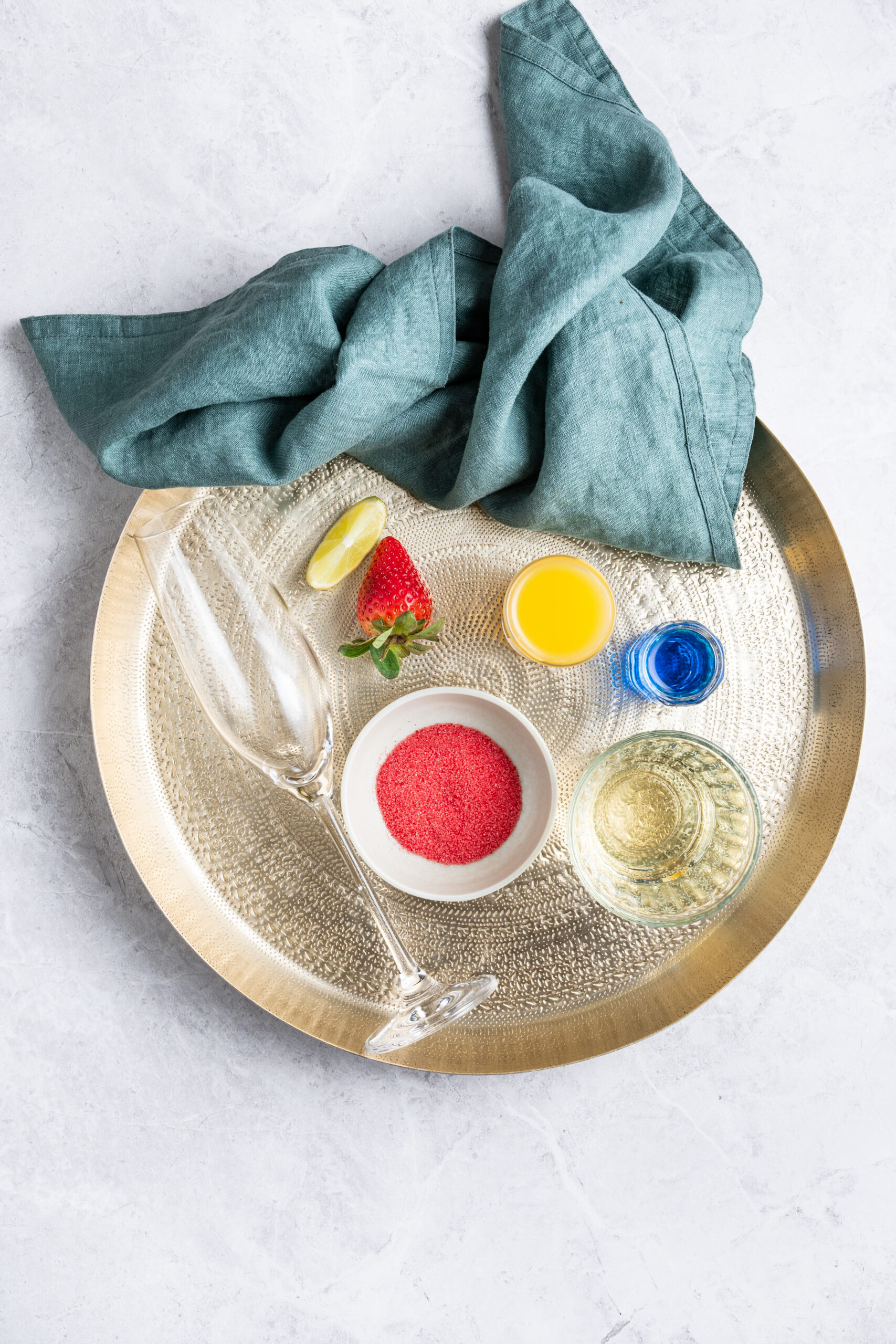Ingredients for Grinch Mimosa: strawberry, lime, red sanding sugar, orange juice, blue cura&ccedil;ao, and sparkling wine.
