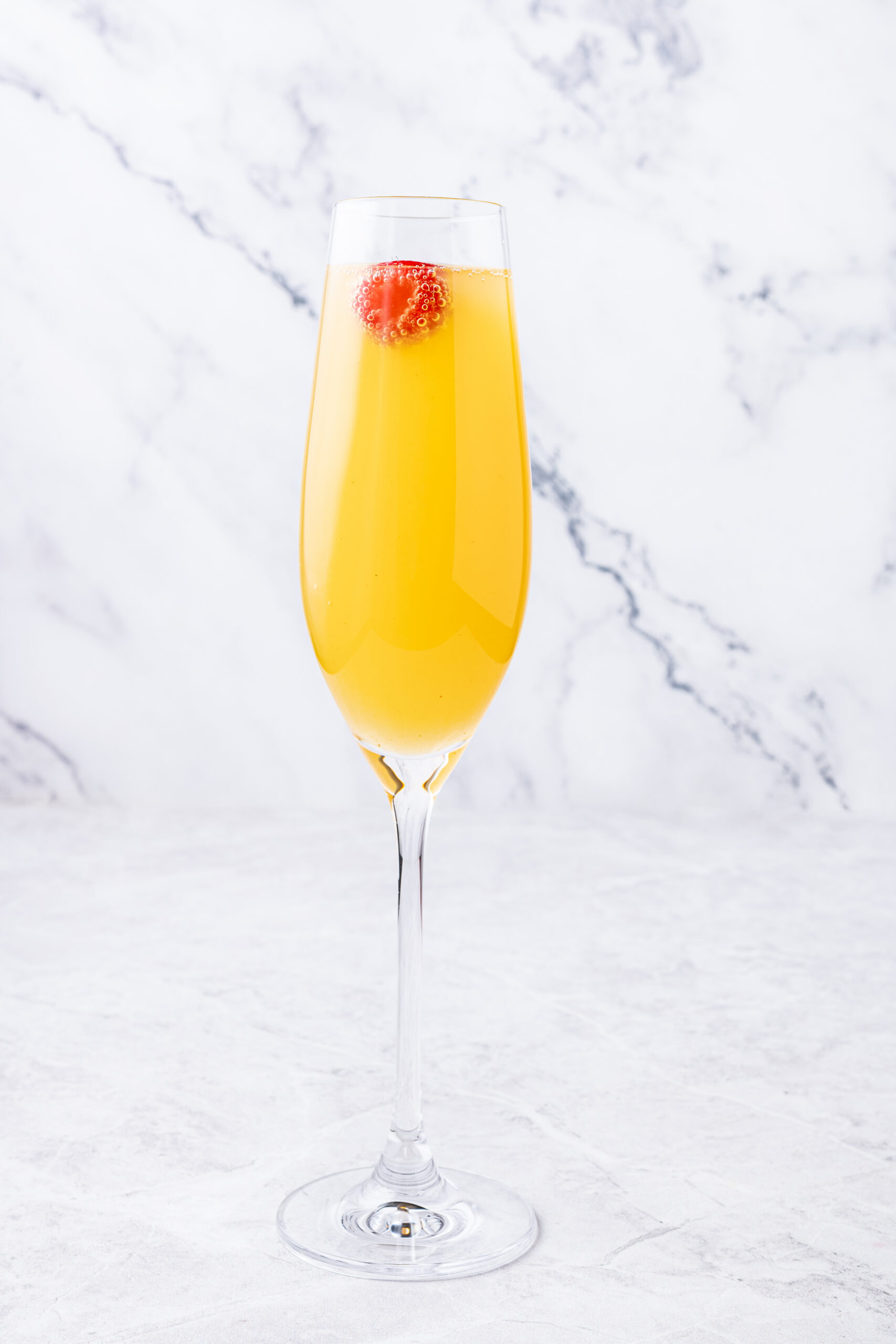 A flute glass containing Peach Mimosa with a raspberry garnish - twistandtoast