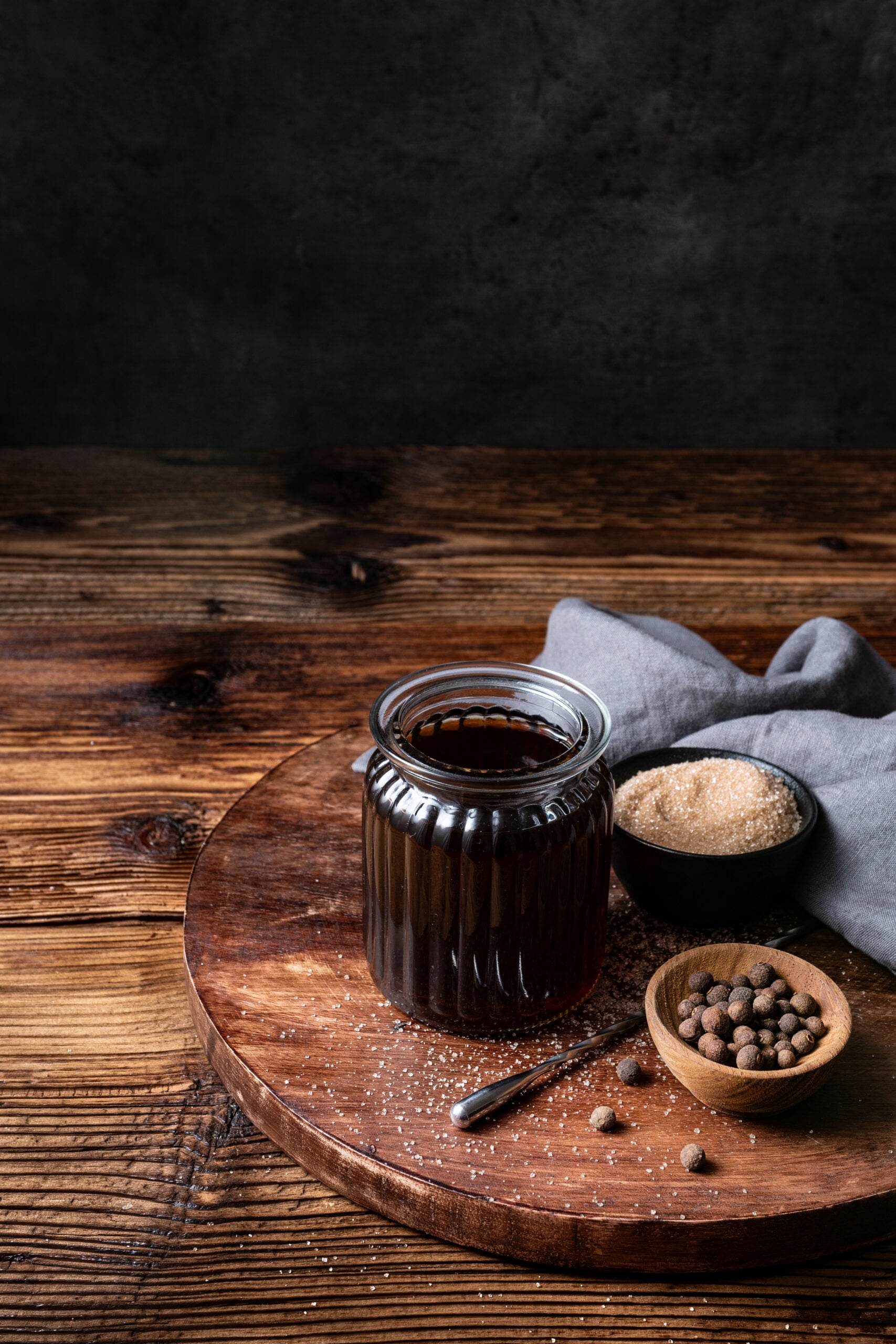 Allspice Dram in a bottle on a tray with allspice berries and powdered sugar diagonal shot