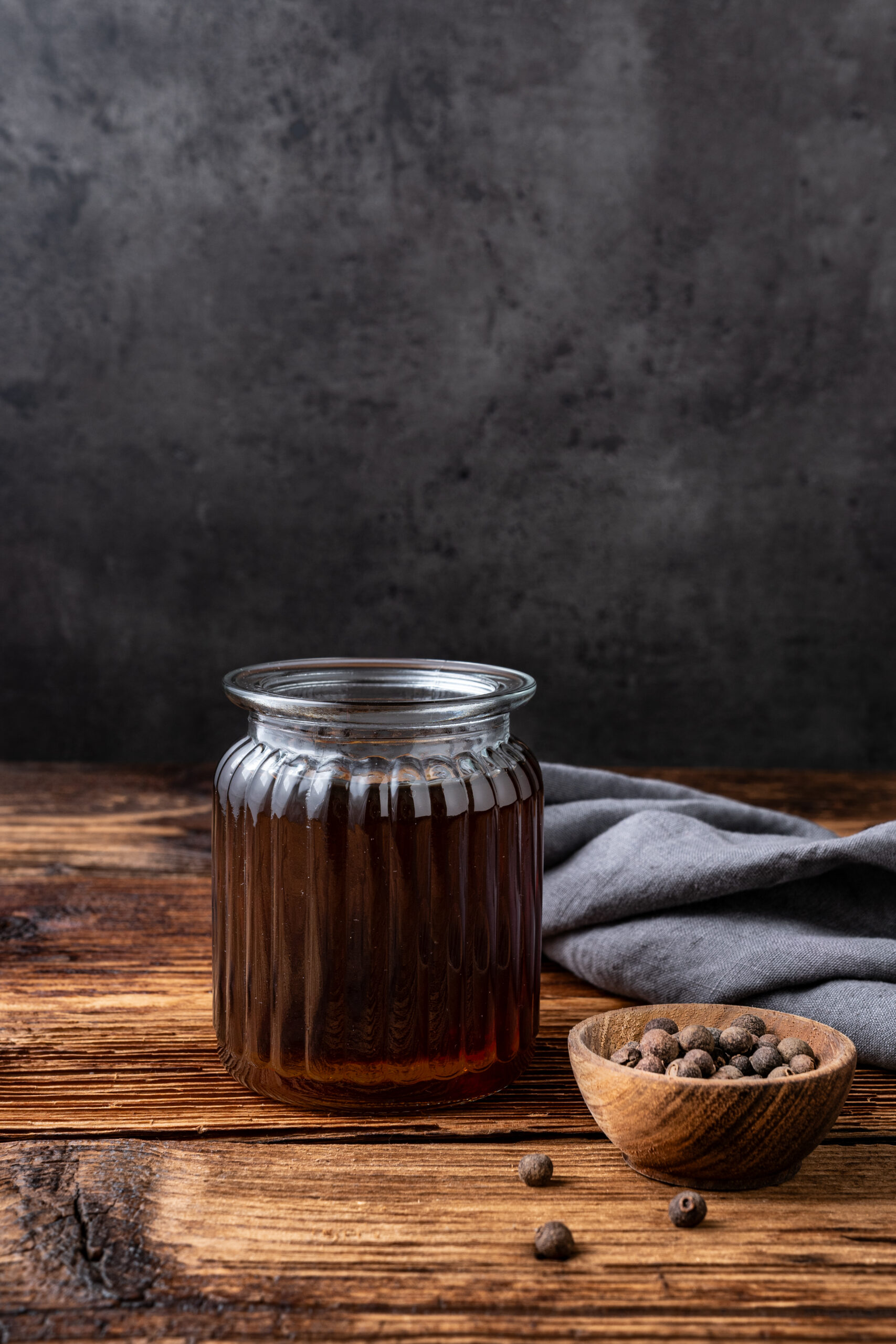 Allspice Dram in a bottle with allspice berries shot from the side