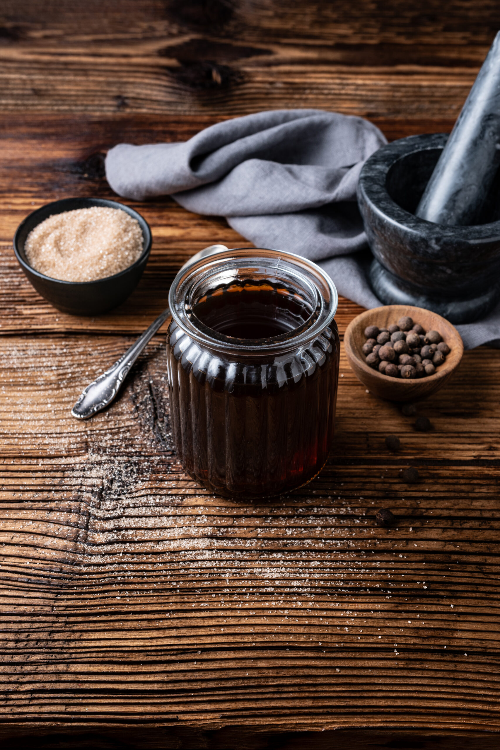 Allspice Dram in a bottle with all spice berries and powdered sugar shot from diagonal